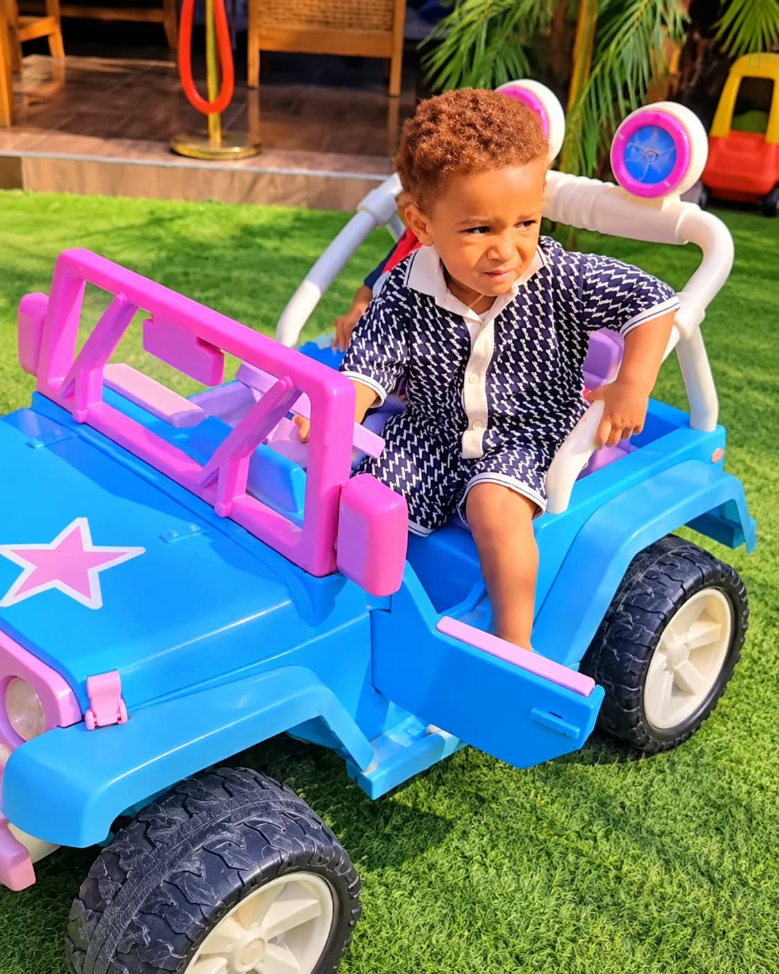 Child enjoying a blue and pink ride-on car on the playground turf